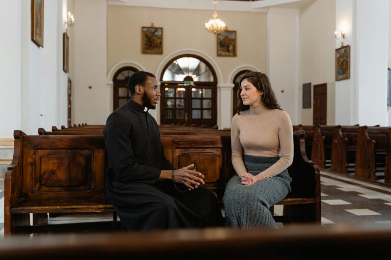 A priest and a woman sit and converse inside a beautifully adorned church.