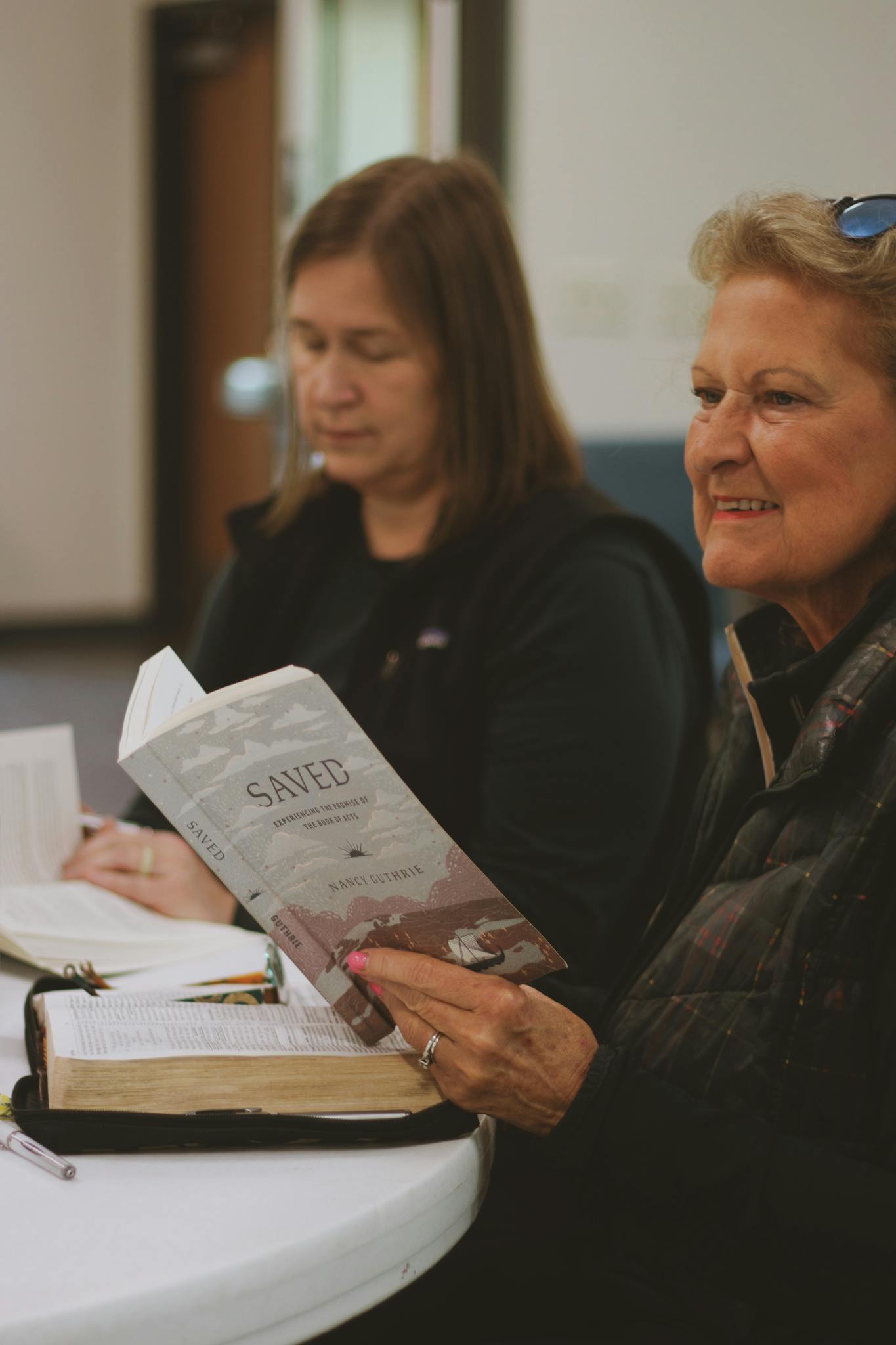 Women gathered around a table studying the Bible and religious texts in fellowship.
